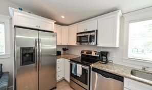 A kitchen with white cabinets, stainless steel appliances, a built-in microwave, a coffee maker, and a dishwasher. - Coconut cottage Unit 1! (Holmes Beach)