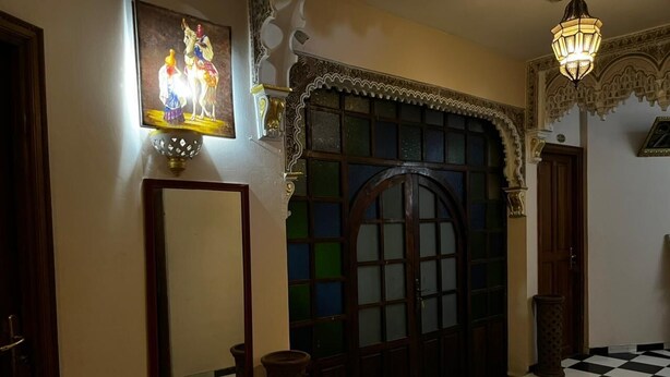 Un couloir doté d’un sol à carreaux, d’un grand miroir, d’une porte décorative et d’un luminaire fixé au mur.