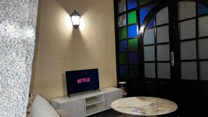 Un salon avec un téléviseur affichant le logo « NETFLIX », un canapé, une table basse et un appliques murales décoratives.