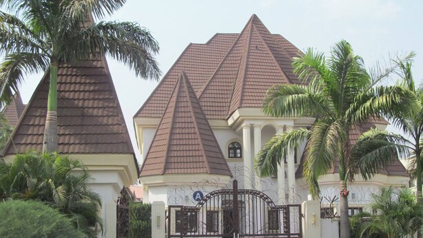 A large, multi-story building with a pyramid-shaped roof, surrounded by palm trees and a gated entrance. - Pauliham Hotel and Suites (Abuja)