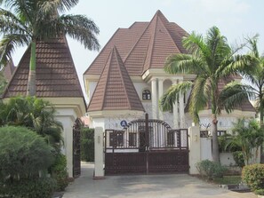 Un edificio grande de varios pisos con techo en forma de pirámide, rodeado de palmeras y una entrada con portones.
