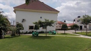 A white building with a red roof, surrounded by a well-maintained lawn and several green chairs. - Pauliham Hotel and Suites (Abuja)