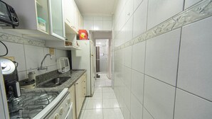 A narrow kitchen with white cabinets, a stove, and a microwave. - Apto com Wi Fi e Garagem a 240 Metros da Praia (Santos)