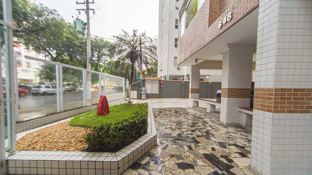 A building with a tiled floor, a small garden area with a red object, and a visible number '646' on the wall. - Apto com Wi Fi e Garagem a 240 Metros da Praia (Santos)