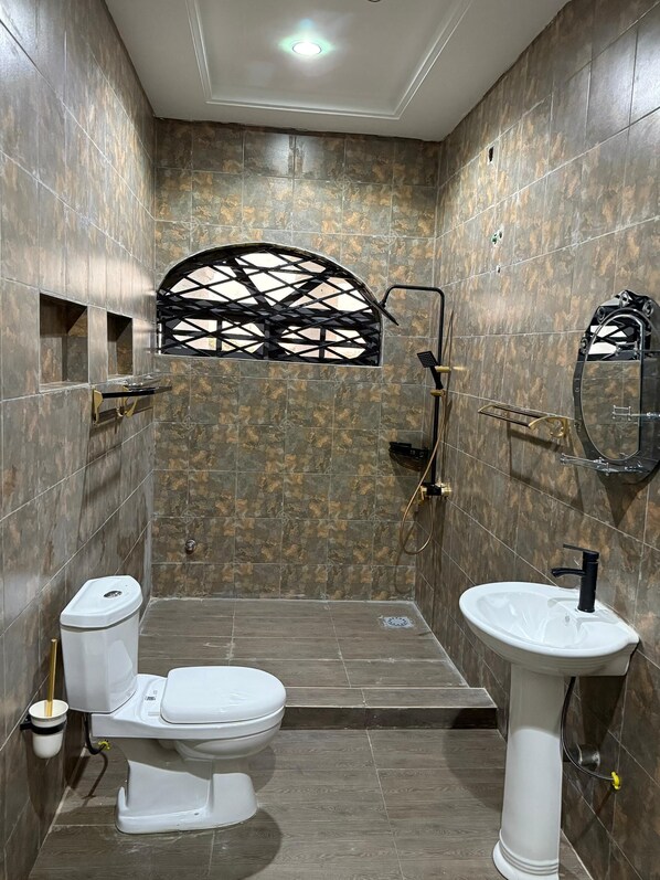 Baño con inodoro, lavabo, ducha y un ventanal decorativo.