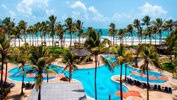 Ein Resort mit großzügigem Poolbereich, Palmen und Blick auf den Strand.