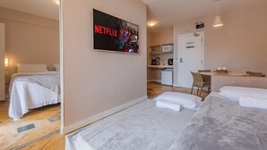 Ein Hotelzimmer mit zwei Betten, einem an der Wand befestigten Fernseher mit Netflix-Logo, einer kleinen Küchenzeile und einem Essbereich mit Tisch und Stühlen.