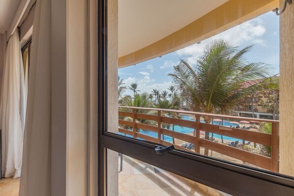Un balcon avec vue sur une piscine, des palmiers et une balustrade en bois.