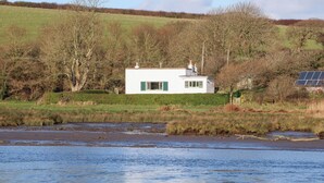 A white building with green shutters, a solar panel, and a river in the foreground. - Bryncyn (Newport)