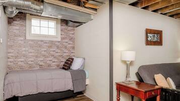 A bedroom with a brick wall, a window, a bed, a nightstand, and a sofa.