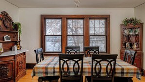 A dining room with a wooden table, chairs, and a chandelier. There are large windows with a view of trees and a snowy landscape. - Waterfront House w/ Patio Near Riverside Park (Kaukauna)
