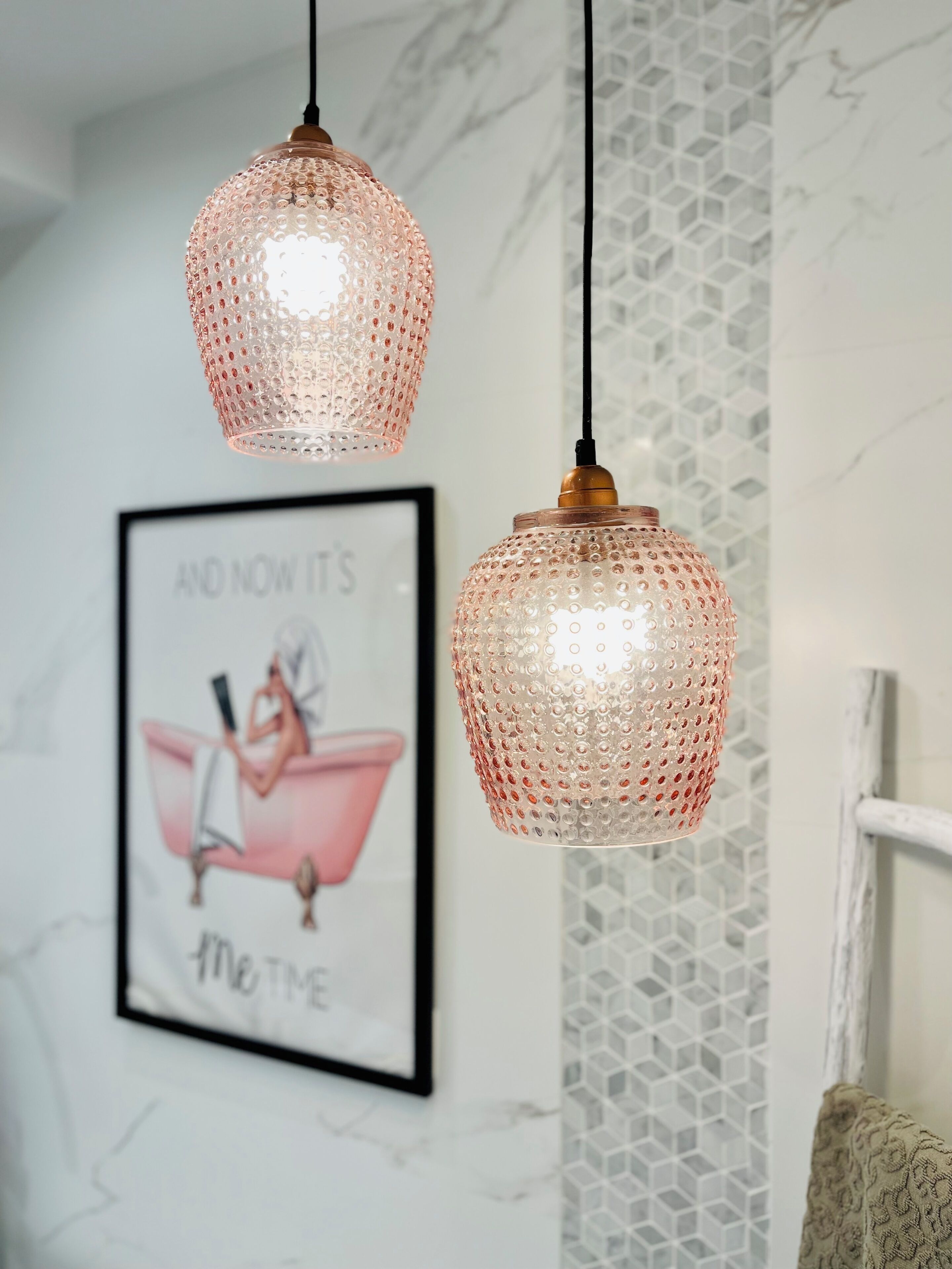 Due lampade pendenti con finiture materiche appese al soffitto, un'illustrazione incorniciata al muro e una sedia bianca con cuscino decorato.