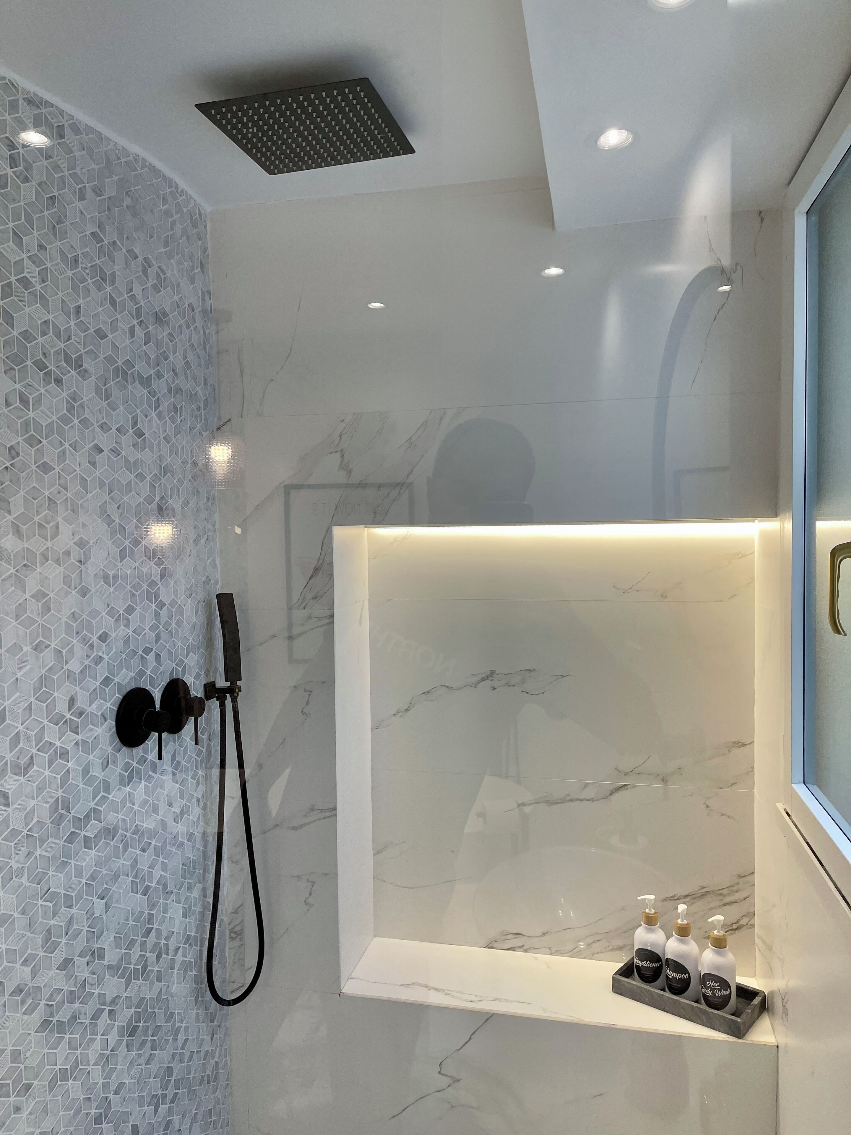 Un baño moderno con cabina de ducha de vidrio, tocador de mármol y repisa con artículos de aseo.