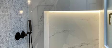 Une salle de bain moderne avec une douche à parois de verre, un meuble-lavabo en marbre et une étagère contenant des articles de toilette.