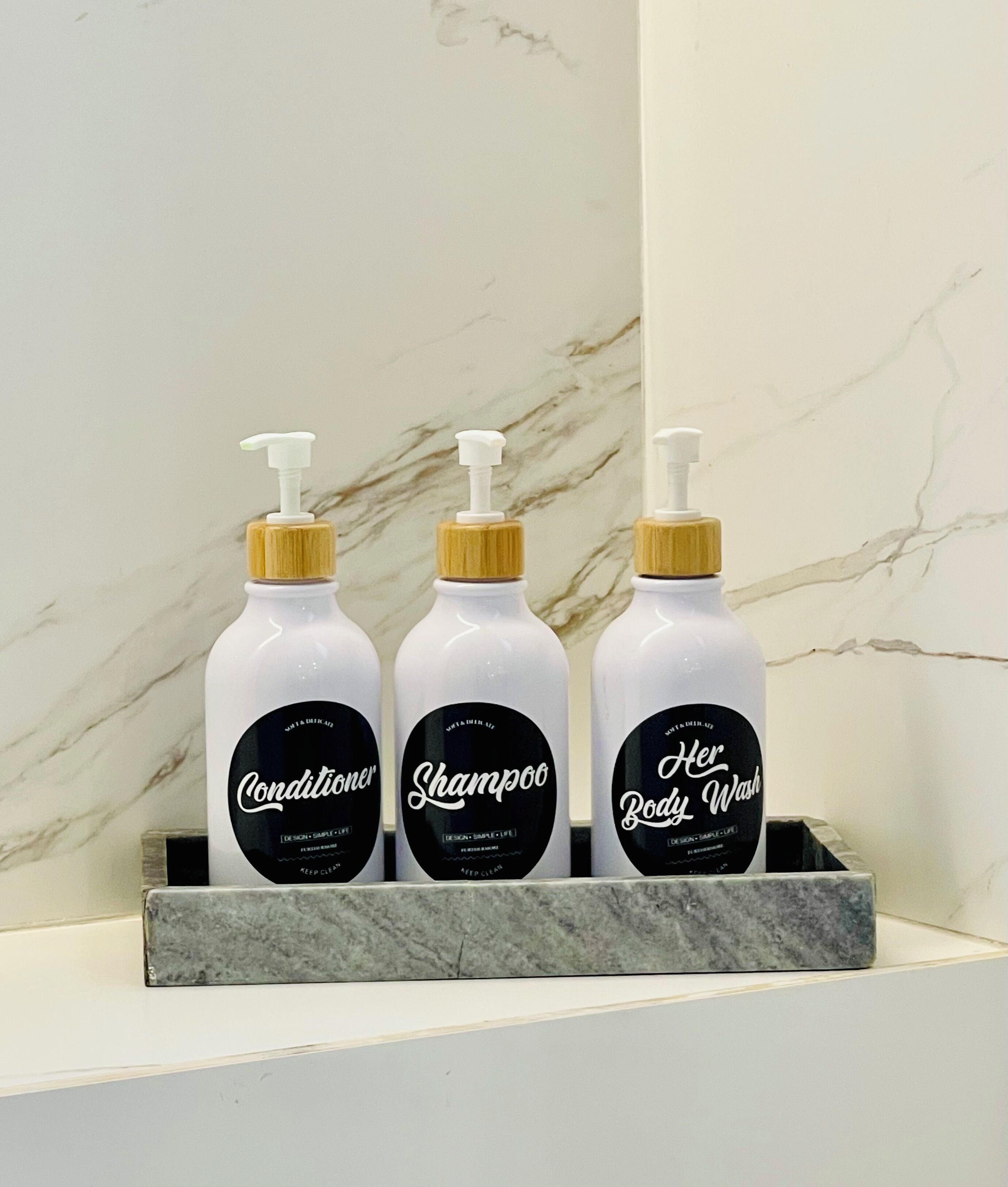 Trois flacons d’après-shampoing, de shampoing et de gel douche, posés sur une étagère en marbre.