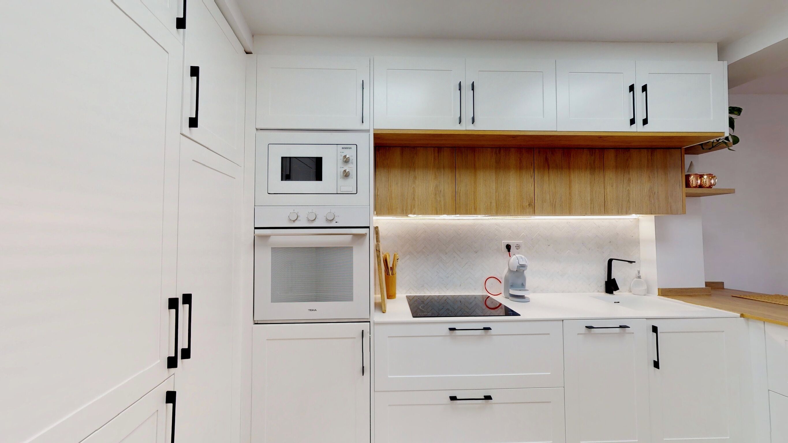 Une cuisine moderne avec des meubles blancs, un four encastré, un four à micro-ondes et un plan de travail en bois.