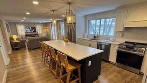 Una cocina moderna con una isla central, sillas de madera, horno empotrado e iluminación colgante.