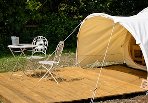Une tente dotée d’une terrasse en bois, d’une table en métal et de deux chaises en métal.
