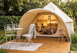 A tent with a bed, a table, and a chair set up on a wooden deck.