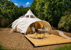 A white tent with a wooden deck and metal chairs.