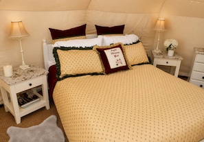 Une chambre confortable avec un lit, des oreillers, une table de chevet, une lampe et une petite table sur laquelle est posé un vase.