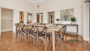 A dining area with a wooden table and chairs, a painting, and a potted plant. - Central Charm - the best of Echuca living! (Echuca)