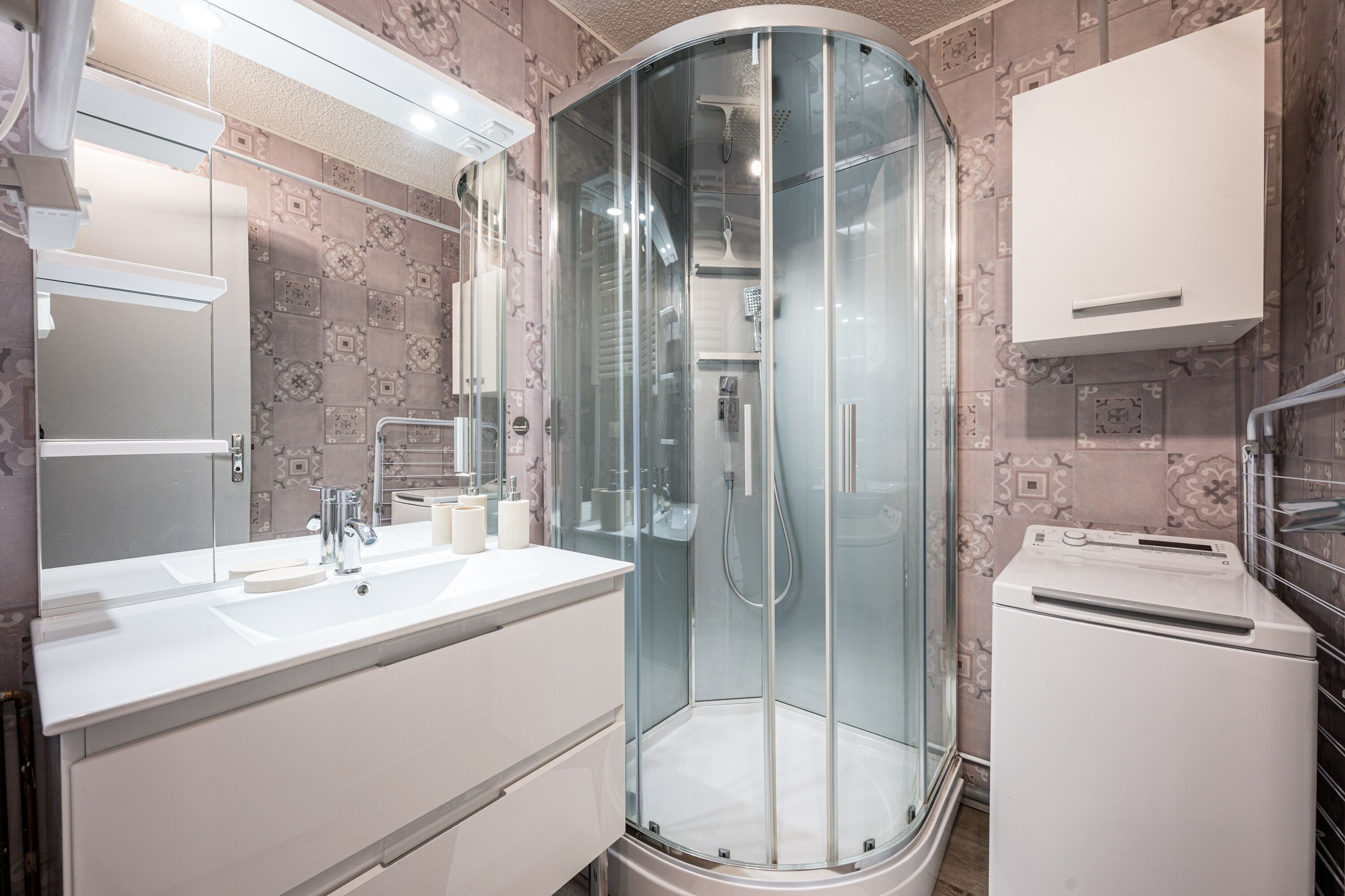 A modern bathroom with a glass-enclosed shower, a white vanity with a mirror, and a built-in washing machine.