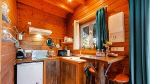 A compact kitchen with wooden walls, a refrigerator, a microwave, a sink, and a window with curtains. - Le Studio Bleu - Jacuzzi Privé (Correns)