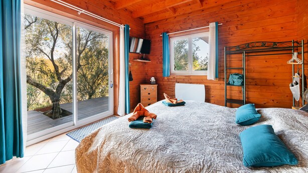 A wooden cabin bedroom with a large bed, a TV, and a sliding glass door leading to a balcony. - Le Studio Bleu - Jacuzzi Privé (Correns)