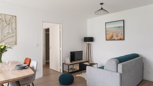Ein modernes Wohnzimmer mit grauem Sofa, einem Esstisch mit Stühlen, einer TV-Konsole und einem Bild an der Wand.