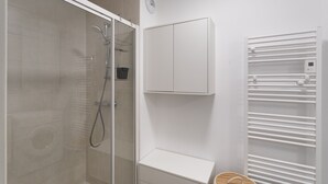 Ein modernes Badezimmer mit einer gläsernen Duschkabine, einem weißen Waschtisch mit Spiegel und einem Handtuchhalter.