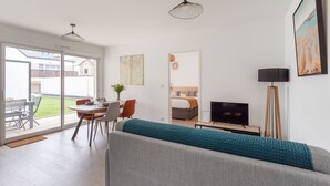 Ein modernes Wohnzimmer mit einer Couch, einem Esstisch und einem Fernseher. Es gibt einen Balkon mit Blick ins Freie.