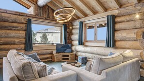 L’intérieur d’une cabane en rondins, avec un ensemble de canapés, un téléviseur et un meuble de rangement en bois.