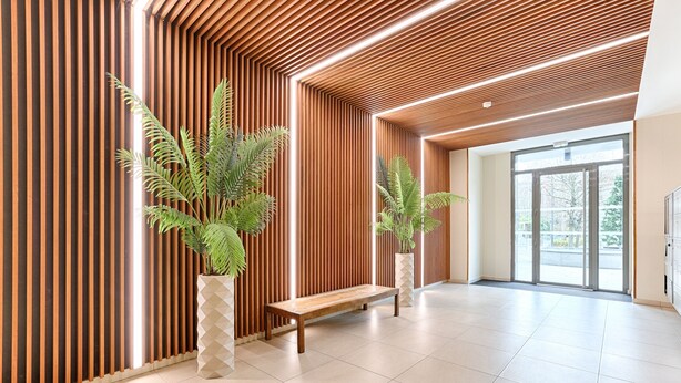 Eine moderne Lobby mit Holzlamellenwänden, einer Bank und Topfpflanzen.