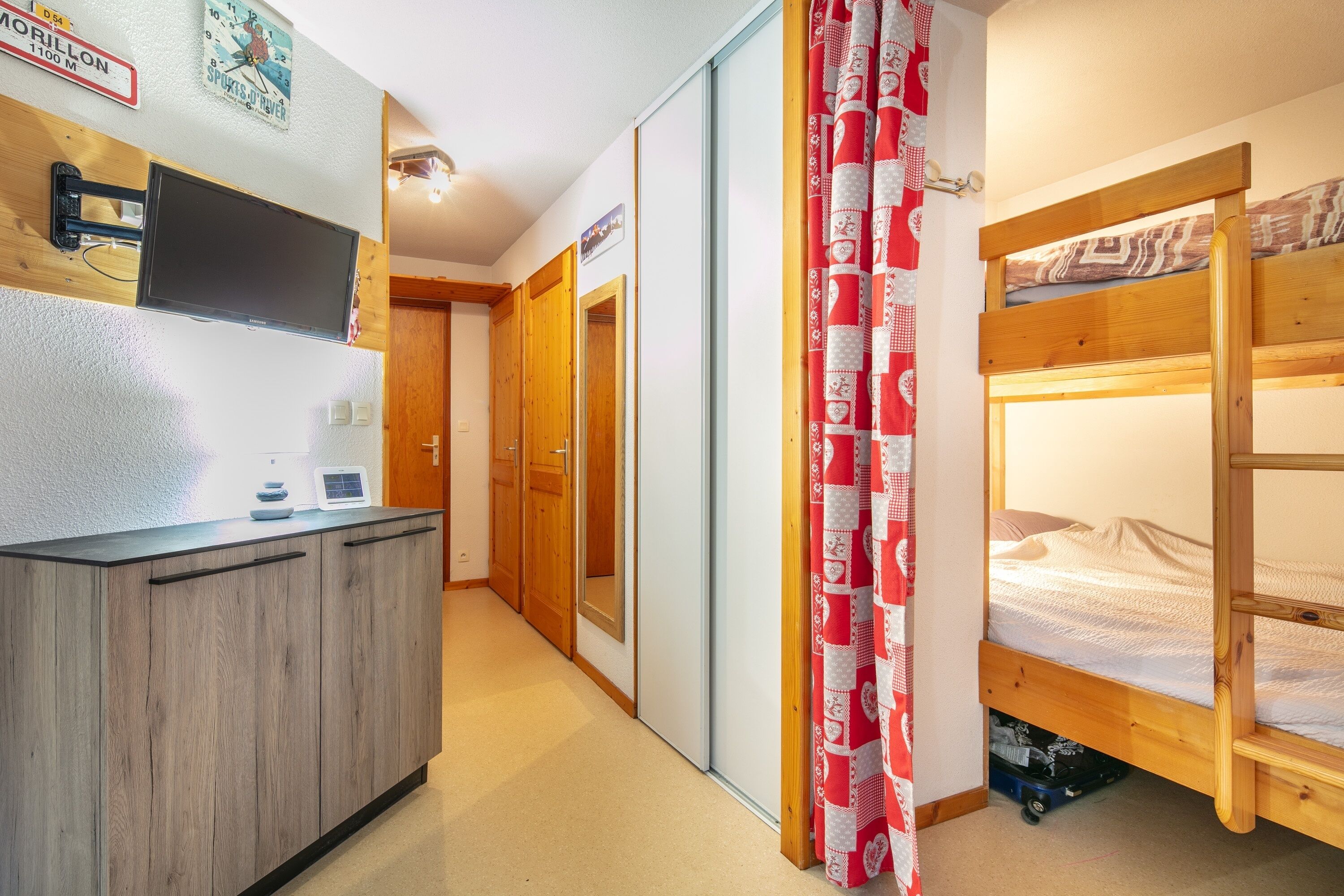 Ein kleines Zimmer mit einem Etagenbett, einem Holztisch mit Flachbildfernseher und einem Schiebetürenschrank.