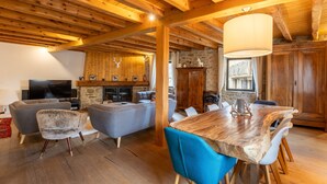A spacious living area with a wooden ceiling, a stone fireplace, and a dining table with chairs. - L’Écrin des Angles - Jacuzzi, Sauna, Hamman privé (Les Angles)
