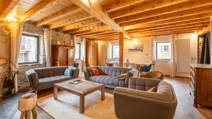 A spacious living room with wooden beams, a stone wall, and a fireplace. There are multiple sofas and a coffee table. - L’Écrin des Angles - Jacuzzi, Sauna, Hamman privé (Les Angles)