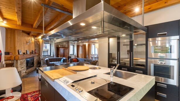 A modern kitchen with a large island, stainless steel appliances, and a stone fireplace. - L’Écrin des Angles - Jacuzzi, Sauna, Hamman privé (Les Angles)