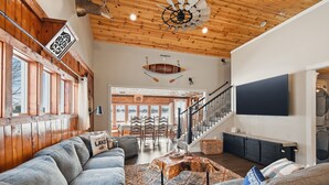 Un salon spacieux doté d’un plafond en bois, d’un grand téléviseur et d’un escalier menant à un niveau supérieur.