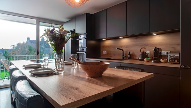 Una cucina moderna con mobili scuri, un piano di lavoro in legno e un'area pranzo con tavolo apparecchiato per quattro.