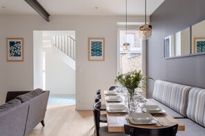A modern dining area with a wooden table set for four, a grey sofa, and a striped bench. - Le Rock Fish - Quelques minutes de la plage (Dinard)