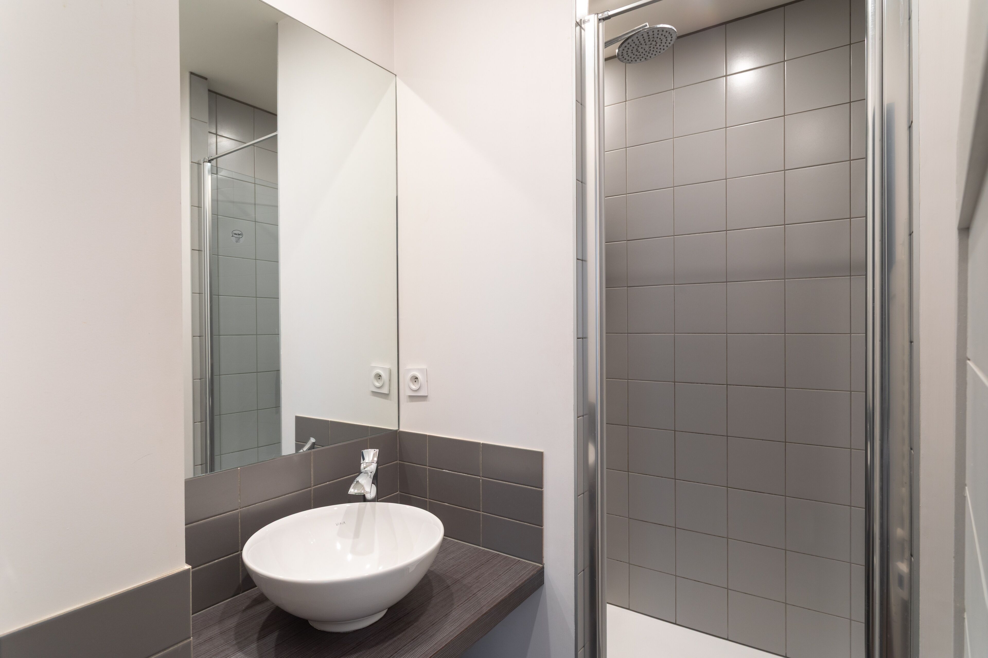 A modern bathroom with a white sink, a large mirror, and a glass-enclosed shower.