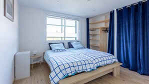 Een slaapkamer met een bed, een bureau, een kledingkast en een raam met gordijnen.
