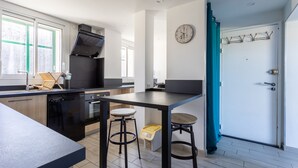 Een moderne keuken met een zwart fornuis, een spoelbak en een aanrecht. Er hangt een klok aan de muur en een deur met een kapstok.