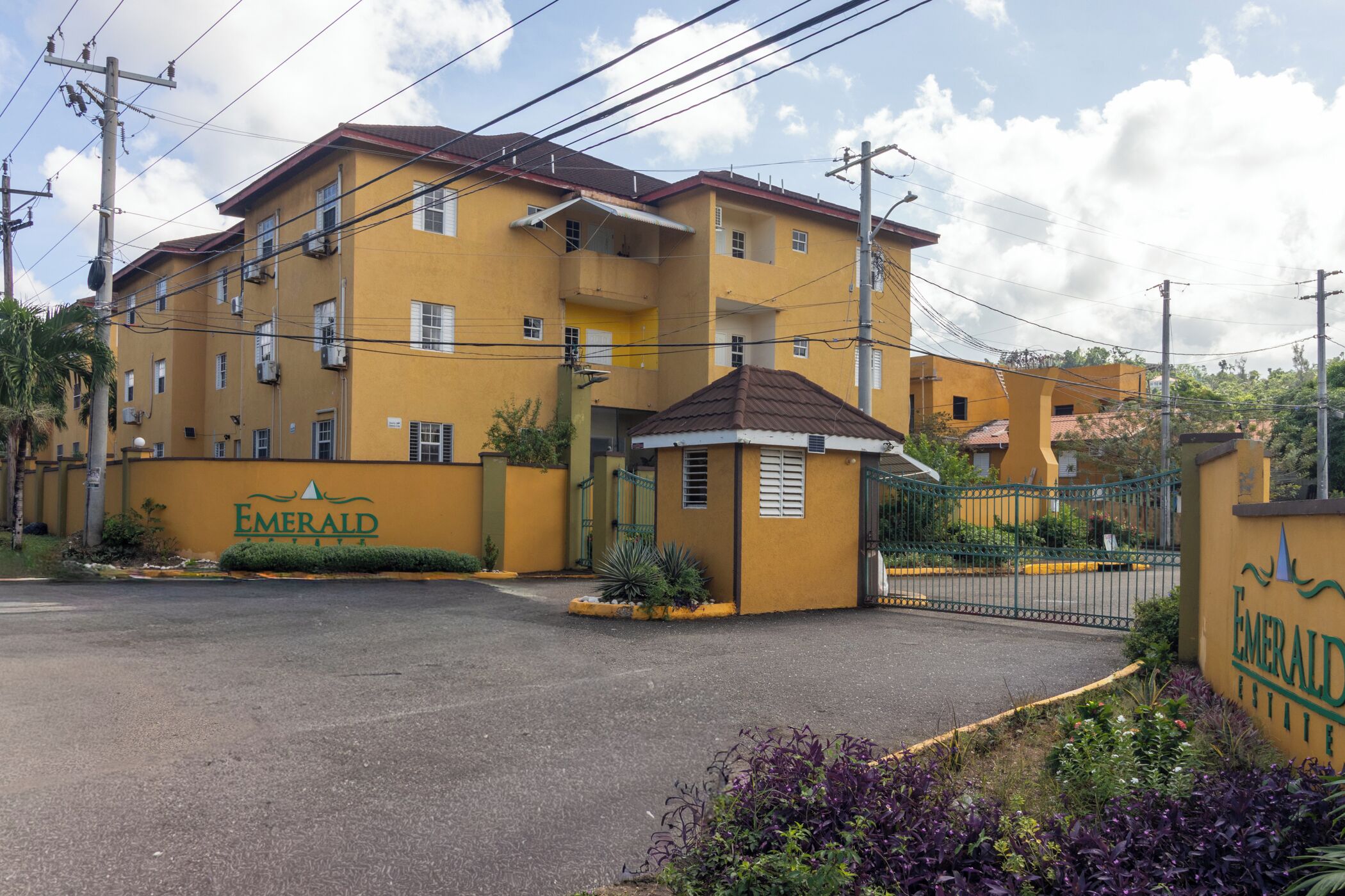 A multi-story hotel with a yellow facade, a gated entrance, and a sign reading "Emerald Suites."
