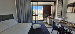A hotel room with a bed, a desk, and a view of the city. - COBAR0143 - Edifício ZN Barra (Salvador)