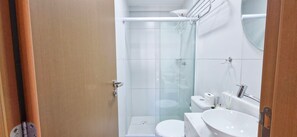 A compact bathroom with a glass shower enclosure, a toilet, and a sink. - COBAR0143 - Edifício ZN Barra (Salvador)