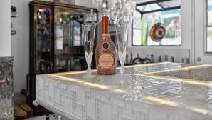 Eine Flasche Cuvée Rose Champagner auf einer Bar, mit zwei Gläsern, einer Kandelaber und einem Schrank im Hintergrund.