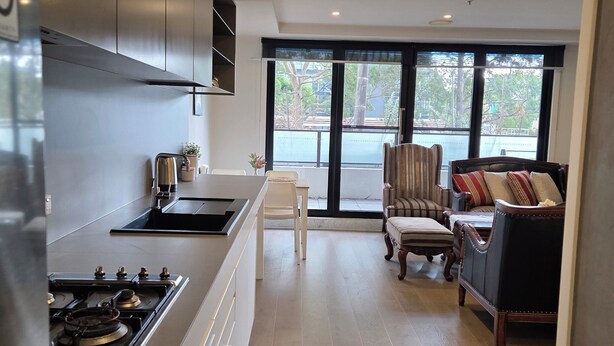 A modern kitchen with a gas stove, a dining area with a table and chairs, and a balcony with a view. - Apartment in Windsor (MELBOURNE)