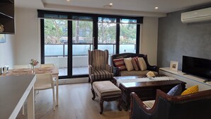 A modern living room with a dining area, large windows, and a flat-screen TV. - Apartment in Windsor (MELBOURNE)